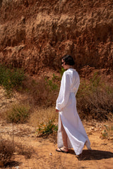 Person in a white dress standing in a desert landscape with a rocky wall in the background